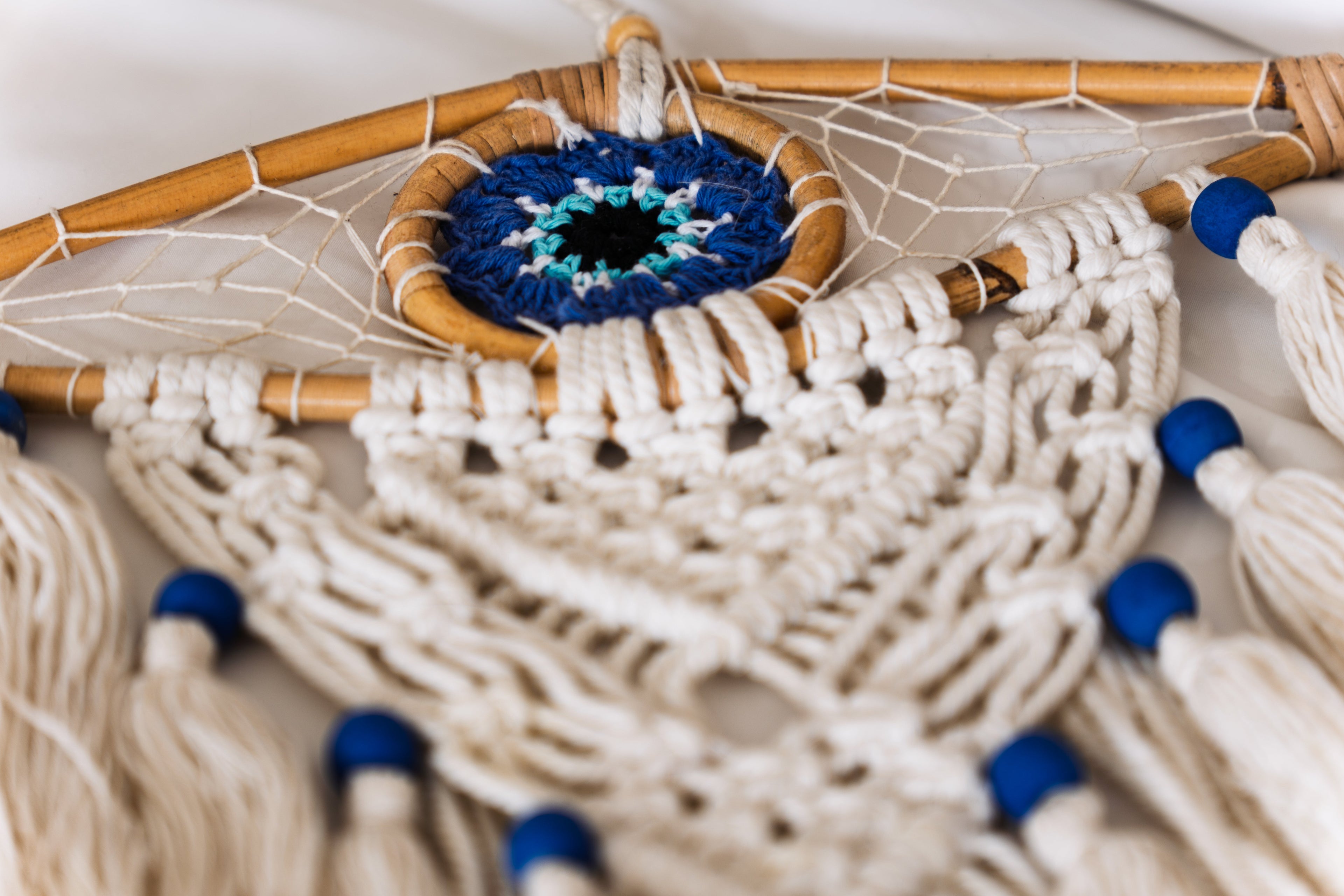 Close up of a wooden dreamcatcher. frame is light clour, tread white and blue. the dreamcatcher is shaped like an eye with a blue iris