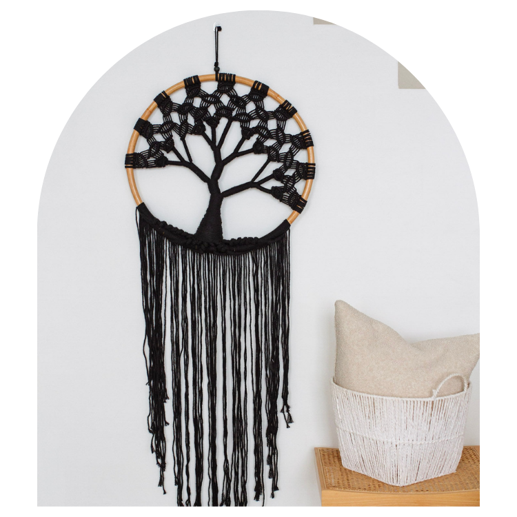 Black tree of life dreamcatcher hanging on a white wall with a basket below.
