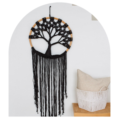 Black tree of life dreamcatcher hanging on a white wall with a basket below.