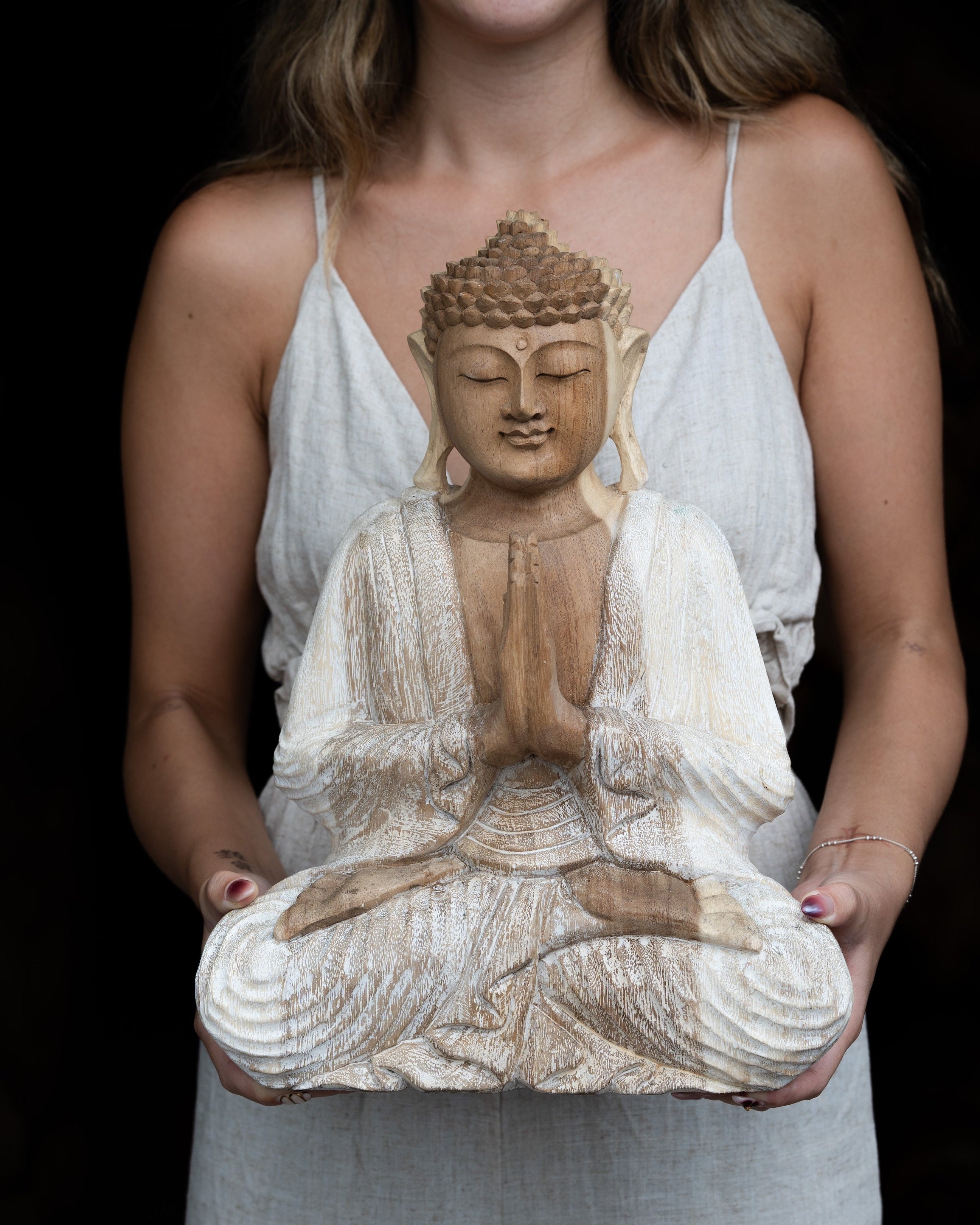 Woman holding a wooden Buddha statue against a black background